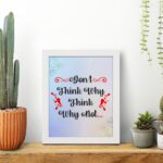 Infidu Don't Think Why, Think Why Not wall art with a red flower design and light blue, light green, and gray background and white frame displayed on the table. Inspiring decor for home offices and workspaces.