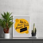 Infidu Take A Small Step Everyday wall art with a gray and yellow background black text and white frame on the table. Inspiring decor for any workspace.