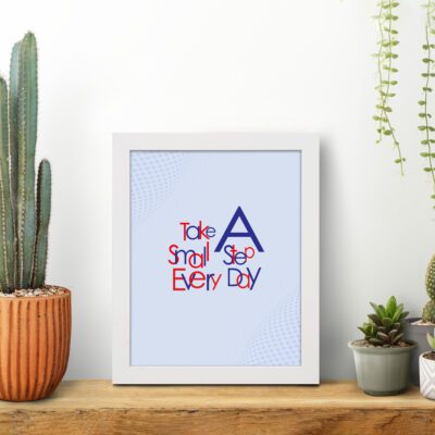 Infidu Take A Small Step Everyday wall art with a gray background navy blue and red text and a white frame on the table. Inspiring decor for any workspace.