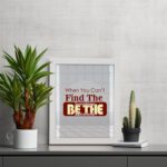 Infidu When You Can't Find The Sunshine Be The Sunshine wall art with a gray and white background and red text and white frame on the table. Inspiring decor for any workspace.