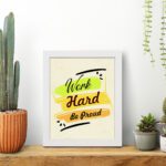 Infidu motivational quotes wall art featuring Work Hard Be Proud on a light white background with light gray flowers and a white frame displayed on the table. the inspiring success