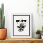 Inspirational quote wall art featuring Believe In Yourself on a white background and white framed on the table. Perfect for motivating your home office.