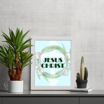 Infidu Jesus Christ Bible Wall Art with JESUS CHRIST text in a mint blue background surrounded by a floral wreath. displayed on the table in a white frame