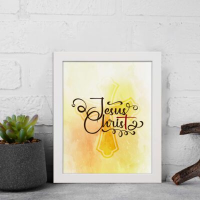 Jesus Christ Bible Wall Art in black script with a yellow cross and watercolor background, framed in black. Perfect Christian home decor. displayed on the wall in a white frame