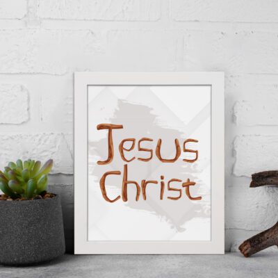 Jesus Christ Bible wall art with hand-drawn brown lettering and a minimalist white-gray watercolor background in a black frame. displayed on the wall in a white frame