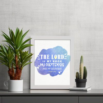 Bible wall art with The Lord Is My Rock, My Fortress, and My Deliverer in white stencil-style text on a blue watercolor background. displayed on the wall in a white frame