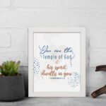 Christian wall art with You are the Temple of God in blue calligraphy and decorative blue dot patterns on a white background. displayed on the wall in a white frame