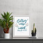 Proverbs 4:7 Christian wall art with elegant script and floral design, featuring Getting Wisdom Is The Wisest Thing You Can Do. displayed on the table in a white frame