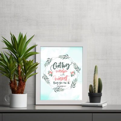 Proverbs 4:7 Bible verse wall art with green leaf wreath and red flowers, perfect for Christian home decor. displayed on the table in a white frame