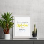 Christian wall art featuring the phrase Your Right Hand Upholds Me in playful fonts with a yellow cursive style and decorative waves. displayed on the table in a white frame