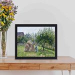 This vintage art print of "Apple Trees in Eragny" by Camille Pissarro,displayed on a table with black frame.