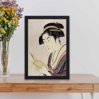 vintage art print features "Kobikicho Arayashiki Koiseya Ochie" by Utamaro Kitagawa, showing a traditional Japanese woman reading a book, framed and placed on the table.