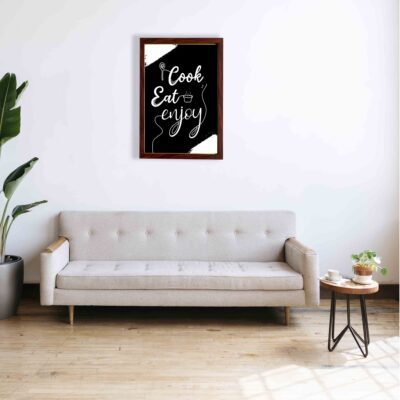 Cook Eat Enjoy Kitchen Wall Art with white cursive text, black background, and kitchen-themed doodles for modern kitchen decor. a sofa below the wall art.