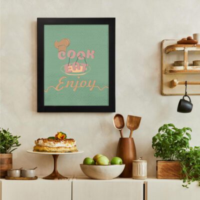 Cook Eat Enjoy kitchen wall art in pastel pink and orange with a light green textured background and a chef's hat. There is a vegetable table, and above it, there is wall art.