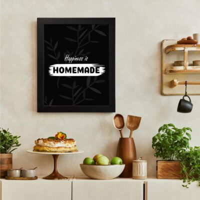 Happiness is Homemade kitchen wall art with white text on a black background and subtle leafy patterns. There is a vegetable table, and above it, there is wall art.