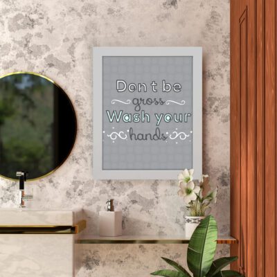 Don't Be Gross Wash Your Hands bathroom wall art with white, black, and mint green text on a light grey grid background with decorative swirls. hung on the wall in the bathroom a white frame