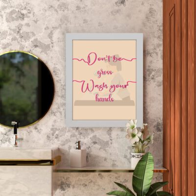 Don't Be Gross Wash Your Hands bathroom wall art with pink cursive text on a light beige background featuring a subtle faucet graphic. hung on the wall in the bathroom a white frame