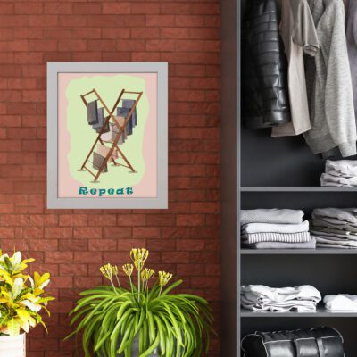 Laundry room wall art with "Repeat" in blue-green text on a light pink background, featuring a wooden drying rack with colorful towels neatly hanging. hung on the wall nearby cupboard