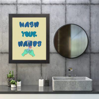 WASH YOUR HANDS bathroom wall art with blue bold text and an illustration of two hands holding soap on a light yellow background. hung on the wall in the bathroom a black frame