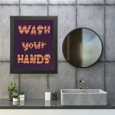 WASH YOUR HANDS bathroom wall art with orange and red text in a checkered pattern on a deep purple background with decorative dots. hung on the wall in the bathroom a black frame