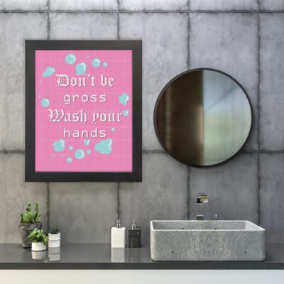 Don't Be Gross Wash Your Hands bathroom wall art with white Gothic text, pink grid pattern, and blue soap bubbles for a playful vibe. hung on the wall in the bathroom a black frame