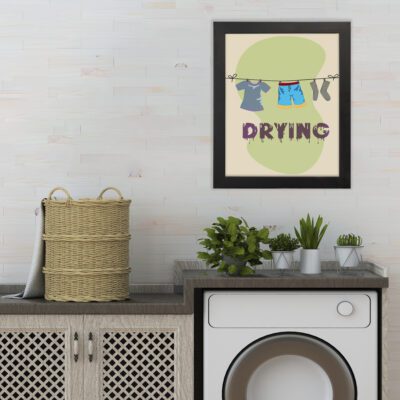 Drying laundry room wall art with a light sandal background, clothes on a clothesline, bold "DRYING" text, and a black frame. hung on the wall the laundry wall art under the washing machine