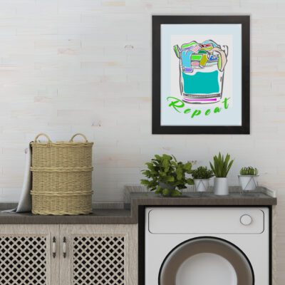 Laundry room wall art with "Repeat" in green cursive text on a light blue background, featuring a bold illustration of a laundry basket overflowing with colorful clothes. hung on the wall the laundry wall art under the washing machine