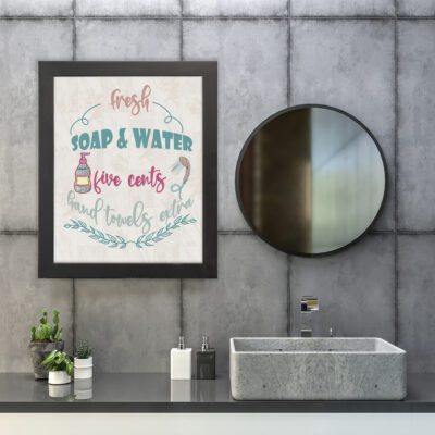 Infidu Fresh Soap & Water bathroom wall art with botanical illustration and green and pink cursive text on a white background. hung on the wall in the bathroom a black frame