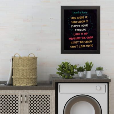 Funny laundry room wall art with bold black background, yellow, pink, and white typography reading "You wear it, you wash it, empty your pockets." hung on the wall the laundry wall art under the washing machine