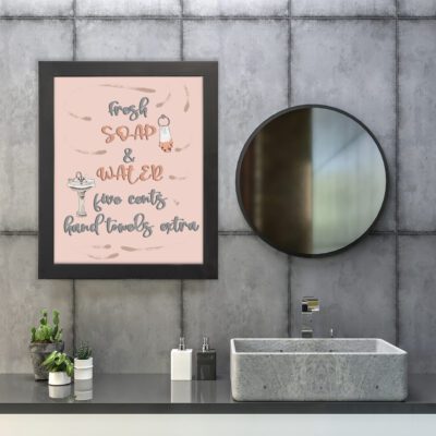 Peach-colored bathroom wall art with the cursive text "Fresh Soap & Water. Five Cents Hand Towels Extra" for a vintage look. hung on the wall in the bathroom a black frame