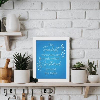 Infidu Happiness is Homemade Kitchen Wall Art with a blue background, white leaf design, and the quote "The fondest memories are made when gathered around the table. displayed on the table