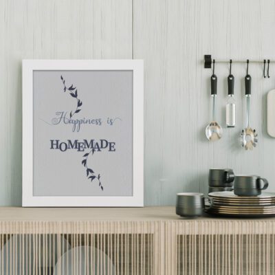 Happiness Is Homemade kitchen wall art with dark blue fonts, leafy vine design, and a light gray background for modern kitchen decor. displayed on the table