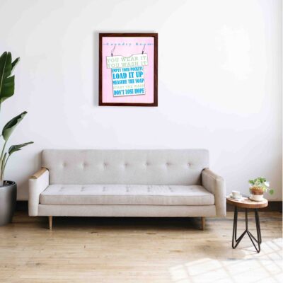 Laundry room wall art with bold blue and gray-green text on a light pink background, featuring a hanger design and funny laundry quotes. a sofa below the wall art.