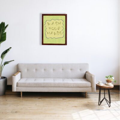 WASH YOUR HANDS bathroom wall art with a light green background, beige wavy text outlined in dark blue, and faint decorative patterns. a sofa below the wall art.