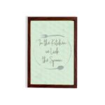 In This Kitchen We Lick The Spoon kitchen wall art with light green background and subtle kitchen utensil pattern in a casual handwritten font. displayed on the wall in a brown frame in a white background