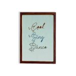 Cook Sing Dance kitchen wall art with hand-drawn fonts, colorful doodles, and a textured light blue background. displayed on the wall in a brown frame in a white background