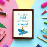 For This Child, We Have Prayed 1 Samuel 1:27 Bible Verse Wall Art with a child on blue bird illustration displayed on the wall in a brown frame in a colorful background