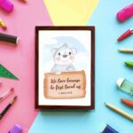 A cute white bear holding a wooden sign with the verse We Love Because He First Loved Us - 1 John 4:19 against a blue sky with clouds. displayed on the wall in a brown frame in colorful background