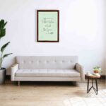 In This Kitchen We Lick The Spoon kitchen wall art with light green background and subtle kitchen utensil pattern in a casual handwritten font. a sofa below the wall art.