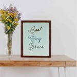 Cook Sing Dance kitchen wall art with hand-drawn fonts, colorful doodles, and a textured light blue background. displayed on the table