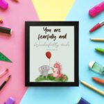 Cute wall art featuring an elephant and dinosaur with the verse You Are Fearfully and Wonderfully Made from Psalm 139:14. displayed on the wall in a black frame in colorful background