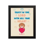 Cute teddy bear holding a heart with Trust in the Lord with all your heart text above, Proverbs 3:5 wall art design. hung on the wall in a black frame