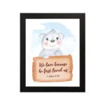 A cute white bear holding a wooden sign with the verse We Love Because He First Loved Us - 1 John 4:19 against a blue sky with clouds. hung on the wall in a black frame