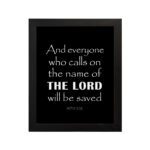 Acts 2:21 Bible wall art featuring bold white text on a black background, reading And everyone who calls on the name of the Lord will be saved. hung on the wall in a black frame