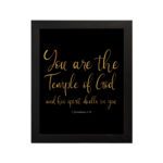 You Are The Temple Of God" Bible Wall Art with gold text on a black background from 1 Corinthians 3:16. hung on the wall in a black frame