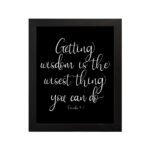 Christian wall art with the quote 'Getting wisdom is the wisest thing you can do' from Proverbs 4:7 in white text on a black background. hung on the wall in a black frame