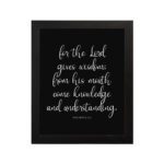 Proverbs 2:6 Christian wall art with white text on a black background – For the Lord gives wisdom design. hung on the wall in a black frame