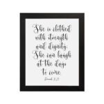 Proverbs 31:25 Christian wall art featuring the text She is clothed with strength and dignity; she can laugh at the days to come. hung on the wall in a black frame