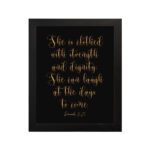 Proverbs 31:25 Christian Wall Art - She Is Clothed With Strength And Dignity, Gold Text on Black Background hung on the wall in a black frame