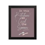 In This Kitchen We Lick The Spoon kitchen wall art with playful spoon illustration on a mauve background. displayed on the wall in a black frame in a white background